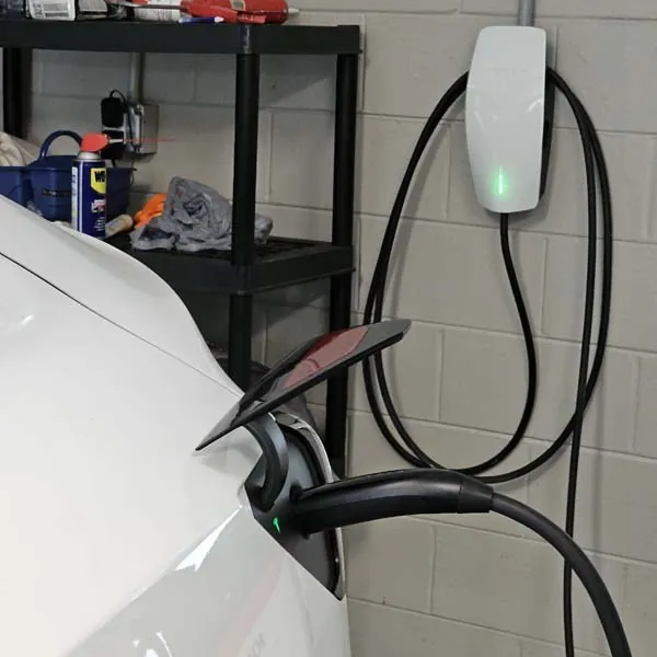 Wall-mounted EV charger plugged into a white car in a garage